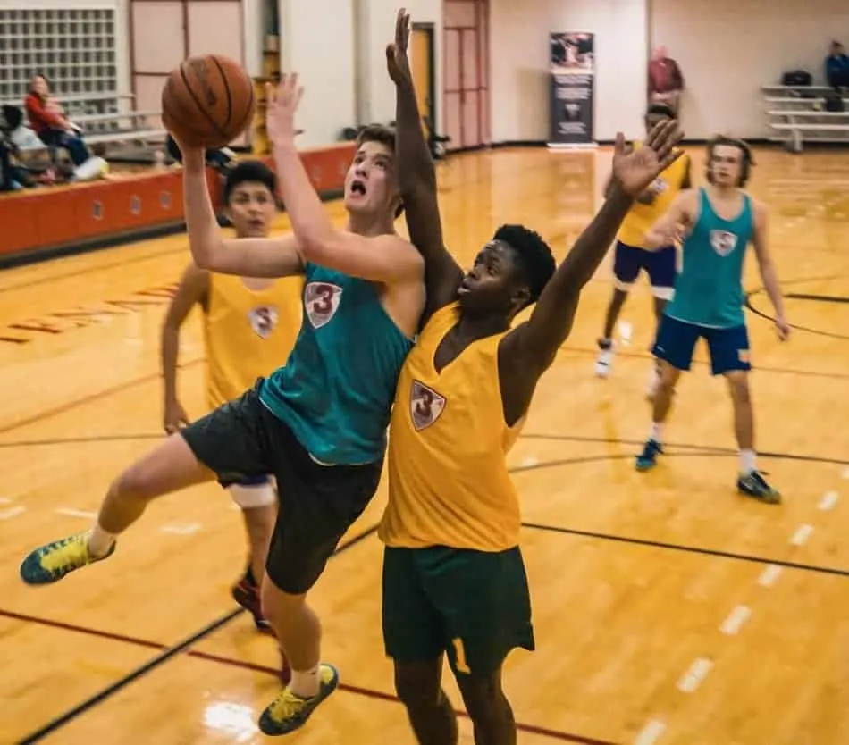 Player in gym going up for a layup in a basketball game, drawing contact.